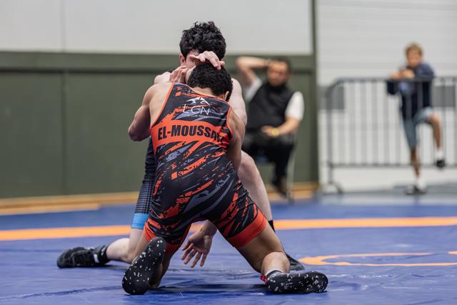 Wrestler El-Moussaed in orange singlet drives opponent to the mat in an intense grappling exchange.