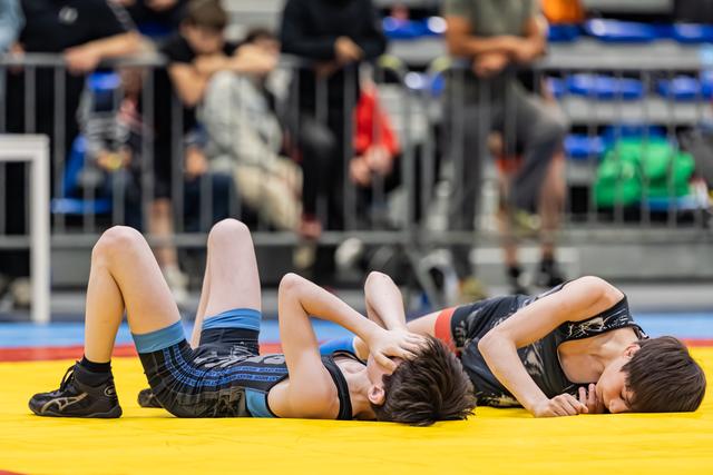 Two young wrestlers battle on a yellow mat, one pinning the other down during an intense youth match.