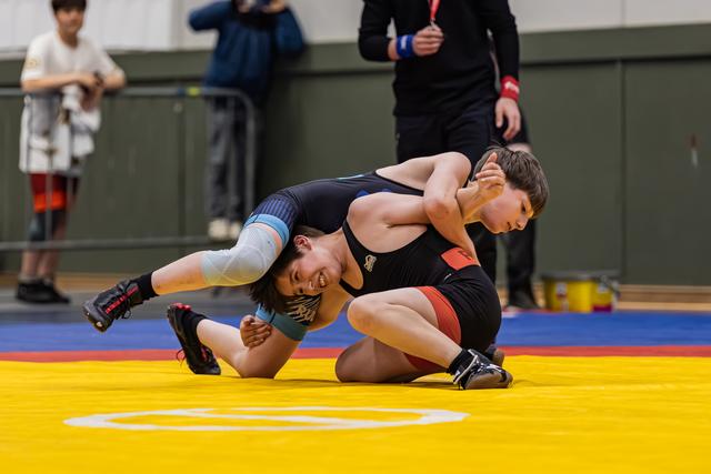 Two young wrestlers battle on a yellow mat, one grimacing as he attempts a takedown during a youth tournament.