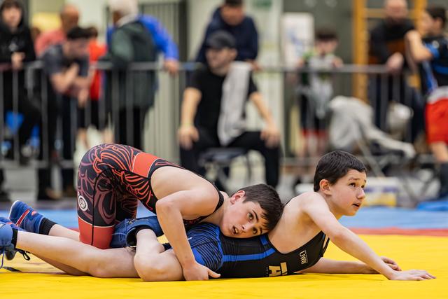 Two young wrestlers compete on a yellow mat, one pinning the other down, both showing intense focus and determination.