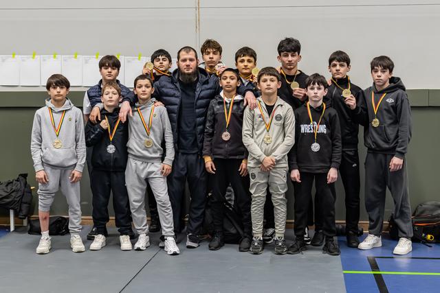 Young wrestlers proudly display gold medals with their coach in a gymnasium after a successful tournament.