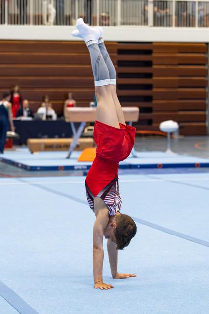 Young athlete performs a handstand on floor exercise mat during indoor training session