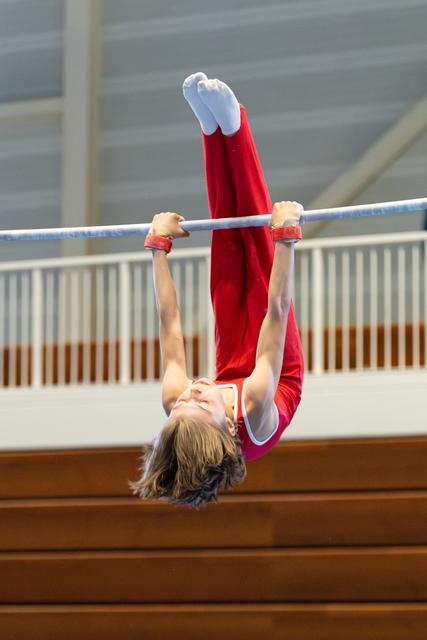 Athlete performs inverted hang on horizontal bar with pointed toes, displaying strength and control during routine