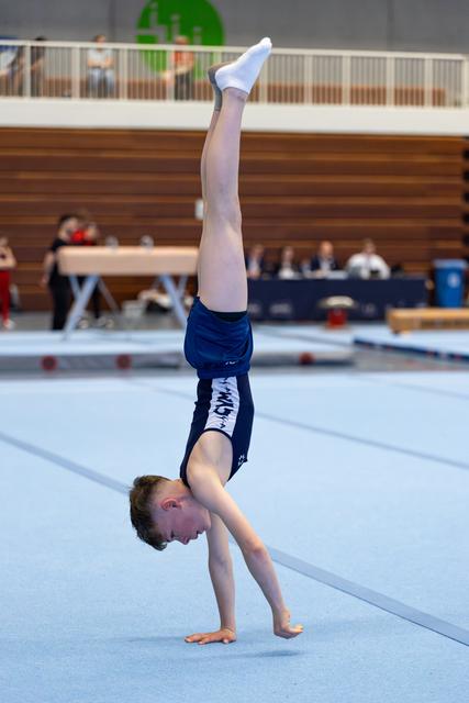 Young athlete performs a handstand during floor exercise routine at indoor gymnastics meet, demonstrating strength and balance