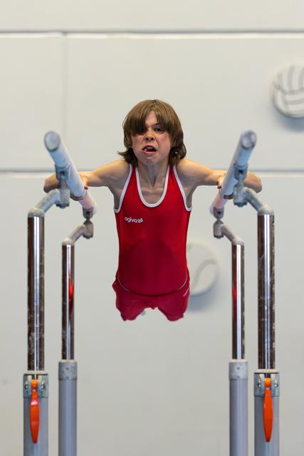 Young gymnast mid-routine on parallel bars, arms extended, showing intense focus and determination during competition