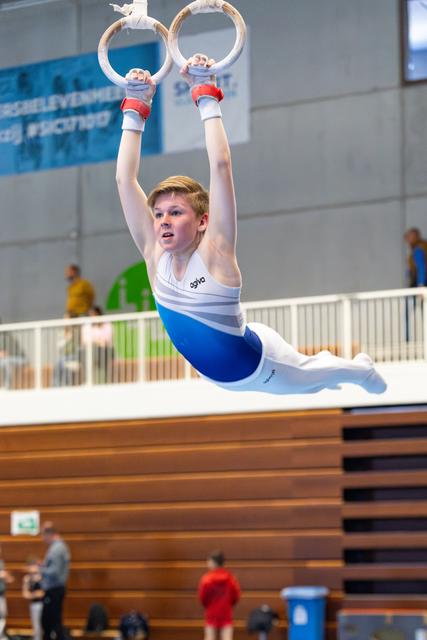 Young athlete performing a strong hold position on still rings during indoor competition, displaying intense focus and strength
