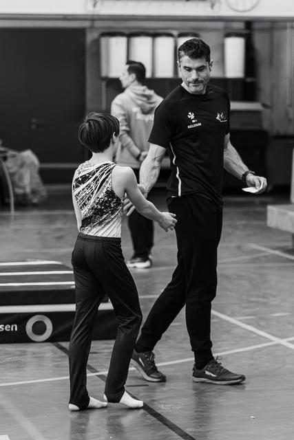 Smiling coach guides young gymnast in sequined leotard during floor exercise practice in training hall