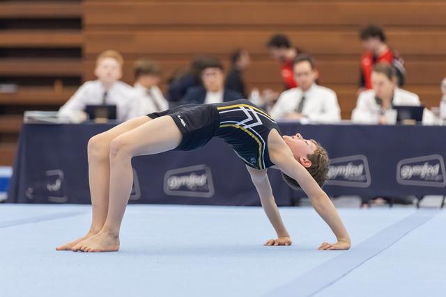 Young gymnast performs a backward bridge pose during floor routine, arching body with hands and feet planted on mat