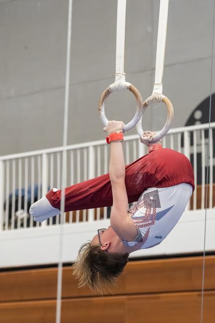 Young gymnast performs inverted position on rings, gripping equipment while upside down in indoor training facility