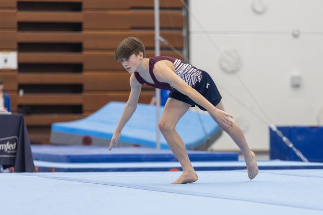 Young gymnast performing floor routine with intense concentration, arms extended in dynamic landing position