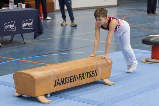 Young gymnast in white and red leotard positions himself at the vault, focused and ready to perform his routine