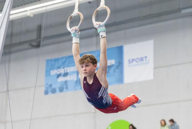 Young gymnast performs on still rings, body horizontal mid-routine, focused expression in bright training facility