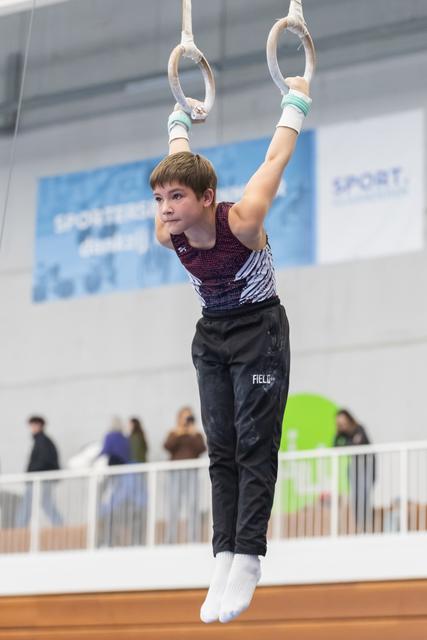 Young gymnast performs on still rings, arms extended overhead, displaying concentration and strength during routine