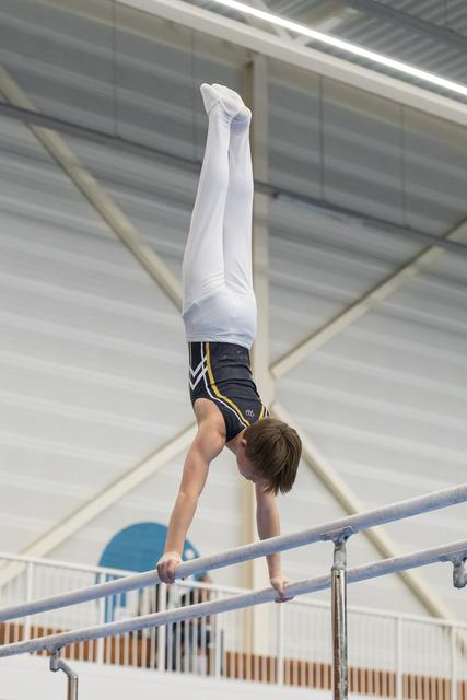 Young gymnast executes a vertical handstand on parallel bars, displaying strength and balance in an indoor training facility