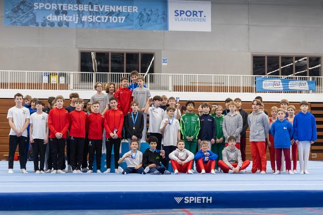 Large group of young gymnasts in team tracksuits pose together with coaches after awards ceremony in indoor sports hall