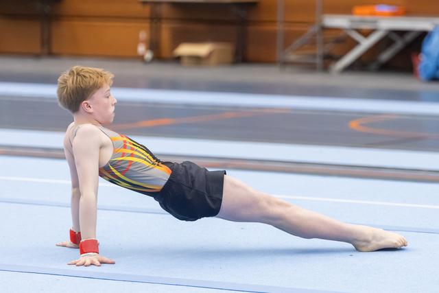 Young gymnast in colorful leotard holds a reverse plank position on the floor mat, demonstrating strength and control