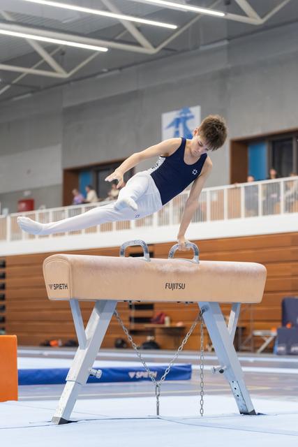 Young male gymnast performs a horizontal support position on pommel horse during training in indoor gymnasium