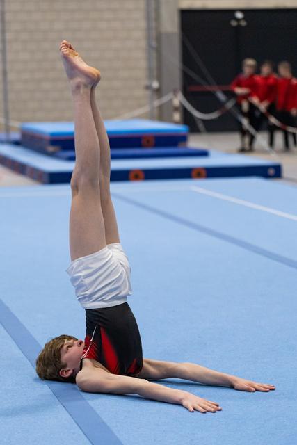 Male gymnast performing a precise leg lift with pointed toe during floor exercise routine at indoor gymnastics facility