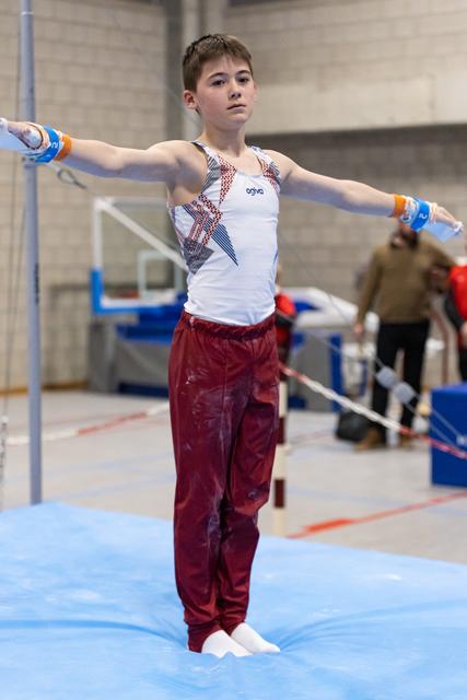 Young gymnast performs on parallel bars with extended arms, wearing maroon pants and white leotard in training facility