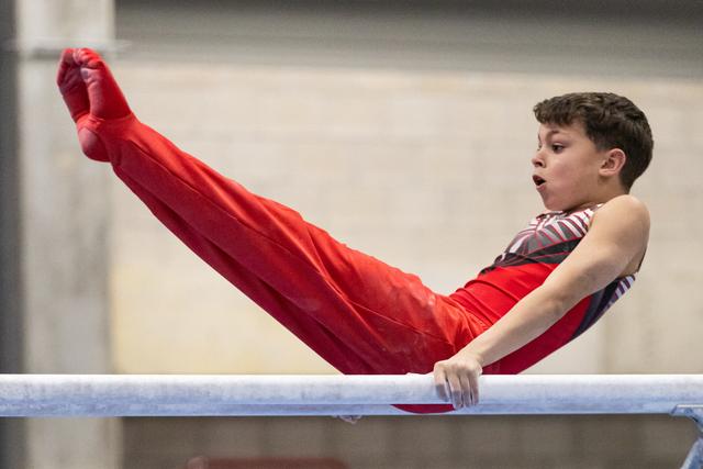 Young gymnast performs a pike position on parallel bars, legs extended upward, displaying strength and concentration