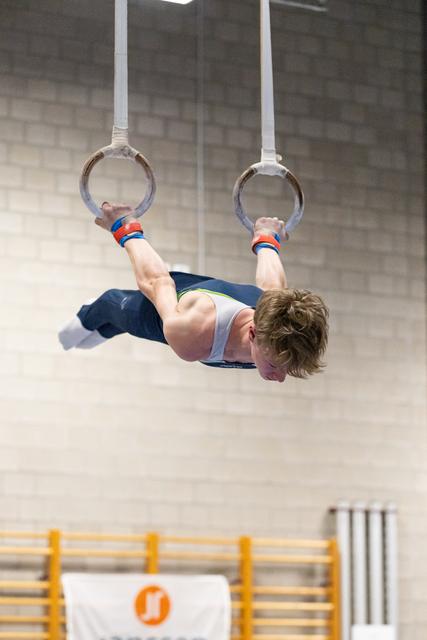 Young gymnast performing an iron cross hold on gymnastics rings, displaying remarkable strength and control in the gym
