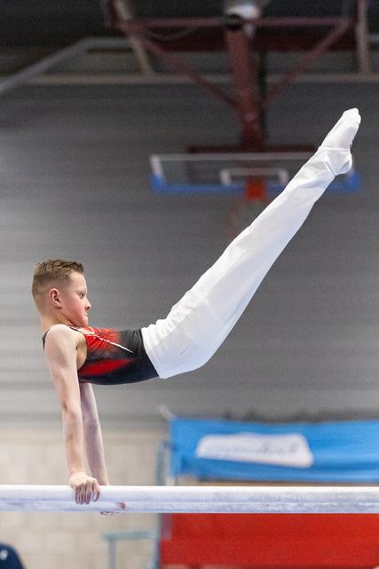 Young male gymnast executes a horizontal hold on parallel bars, legs extended upward, displaying strength and control