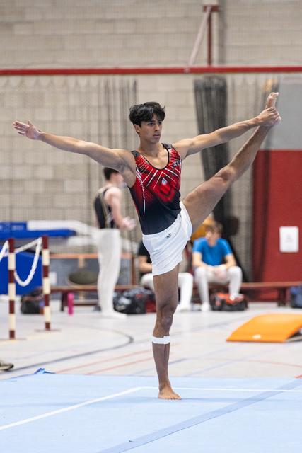 Male gymnast performs an elegant standing leg extension with arms spread wide during floor exercise in training facility