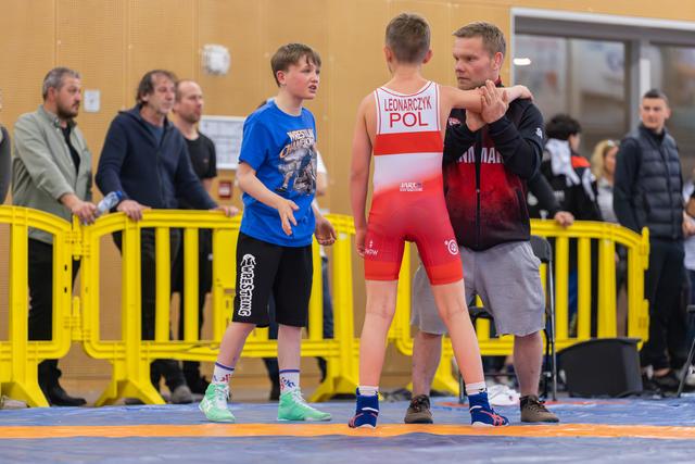 Coach places hand on shoulder of young Polish wrestler (Leonarczyk) while another boy watches on the mat.