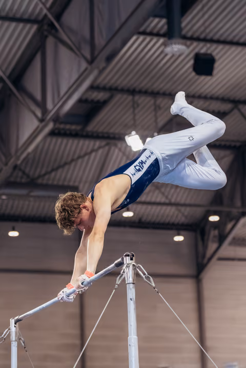 Young male gymnast performs a pike hold on parallel bars, body nearly horizontal, showing intense focus and strength indoors.