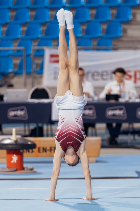 Young gymnast performing a perfect handstand on the floor exercise mat during a gymnastics competition.