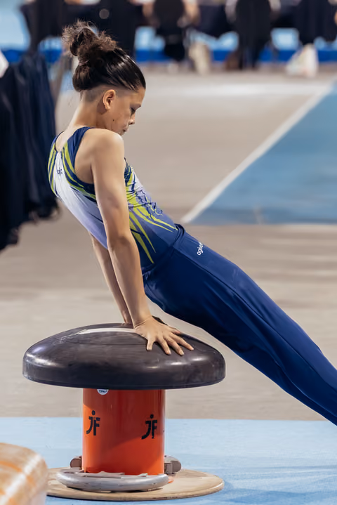 Young female gymnast leans intently over the vault, focused and controlled, during a gymnastics competition.