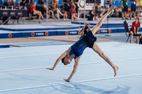 Young gymnast performing a cartwheel on the floor exercise mat, body fully extended, competing at a gymnastics event.