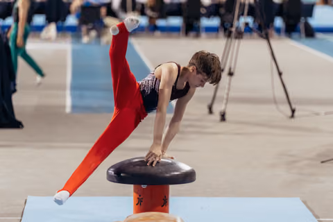 Young male gymnast in red leotard executes a dynamic vault, body extended, intense focus during competition.