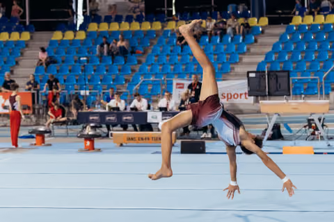 Young male gymnast executes a dynamic airborne back walkover on the floor exercise mat during a gymnastics competition.