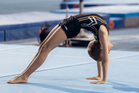 Young male gymnast performs a precise bridge pose on blue floor mat, showing flexibility and focused form.