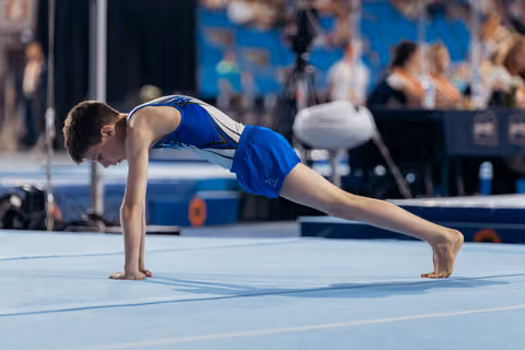 Young male gymnast holds a perfect planche position on the floor exercise mat, showing focused concentration.