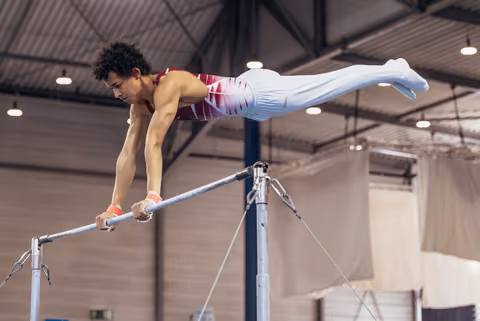 Young male gymnast holds a powerful iron cross position on the horizontal bar, body fully extended, intense focus.