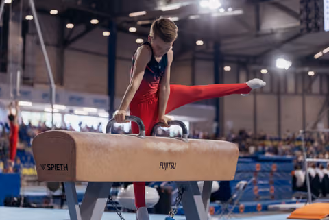 Young male gymnast performs a precise leg split on the pommel horse, concentrating intensely during a competition.