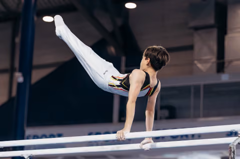 Young male gymnast performs a powerful horizontal hold on parallel bars, legs extended high in a gymnastics hall.