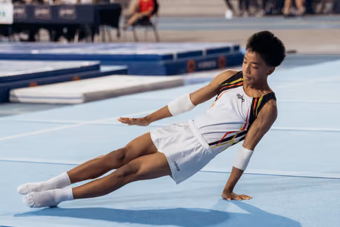 Young male gymnast lands on the floor mat, balancing with one hand, showing focus and composure during his routine.