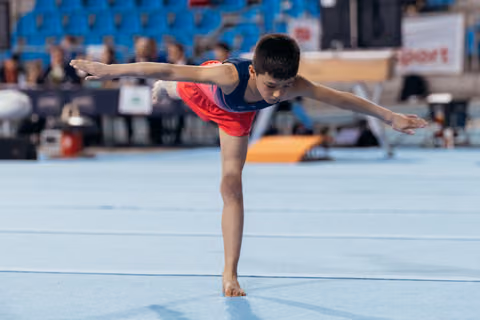 Young male gymnast performs a focused arabesque balance on the floor exercise mat at a gymnastics meet.