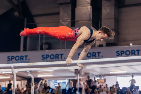 Male gymnast holds a perfect planche on parallel bars, body fully horizontal, intense concentration on his face.