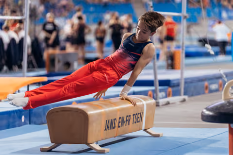 Young male gymnast performs a planche hold on the pommel horse, body parallel to floor, intense concentration during competition.