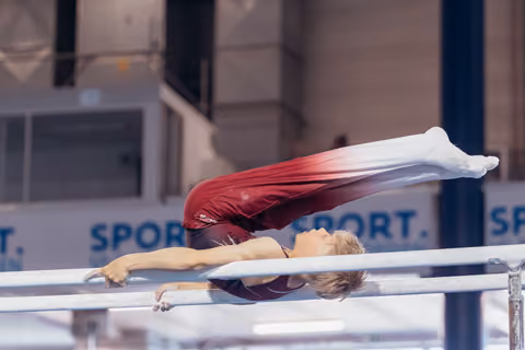 Young male gymnast performs a horizontal hold on parallel bars, body fully extended, in a sports hall.