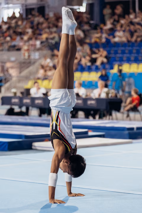 Young male gymnast performs a perfect handstand on the floor exercise mat during a competition, legs straight up.