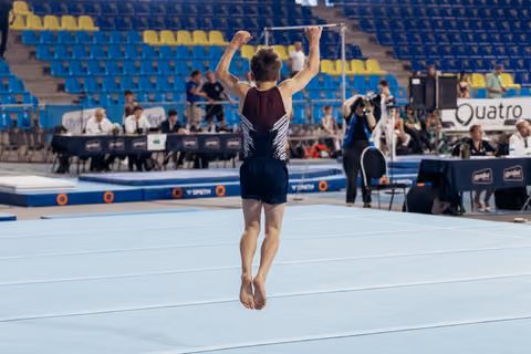 Young male gymnast raises fists overhead in triumph on the floor exercise mat during an indoor gymnastics meet.