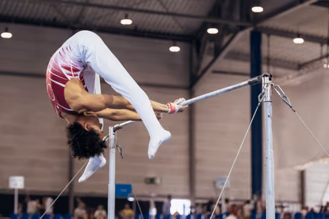 Young gymnast performs a dramatic arch on the uneven bars, body inverted, legs extended, in an indoor sports hall.