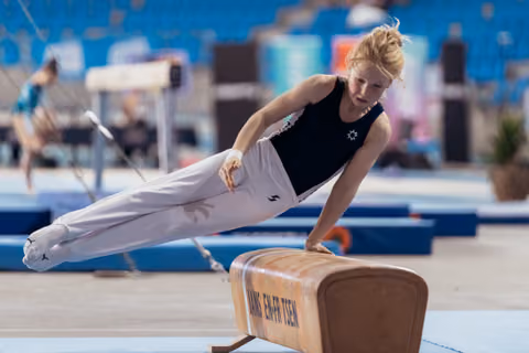Young female gymnast performs a precise pommel horse routine, body fully extended, intense focus in a competition arena.