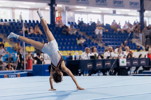 Young gymnast performs a one-handed cartwheel on the floor exercise mat during a gymnastics competition.