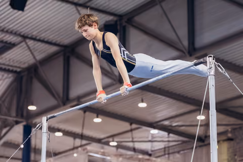Young male gymnast performs on the horizontal bar, body horizontal, intense concentration in an indoor gymnasium.
